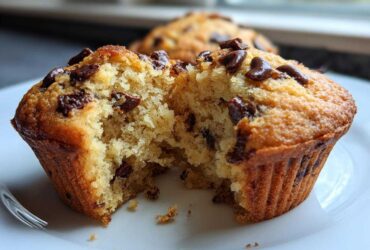 Close-up of a delicious vegan chocolate chip muffin, broken in half to reveal a fluffy interior dotted with chocolate chips.