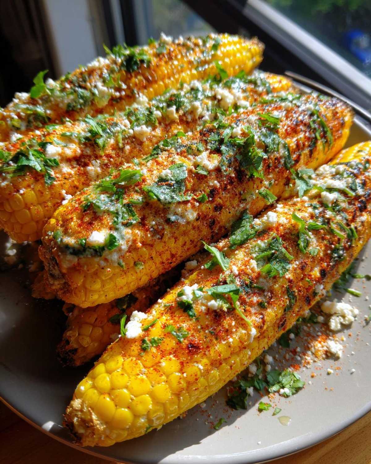 Close-up of grilled Vegan Mexican street corn, generously topped with vegan crema, chili powder, and cilantro.