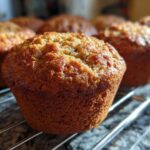 Close-up of golden-brown vegan protein muffins cooling on a wire rack, with more muffins blurred in the background.