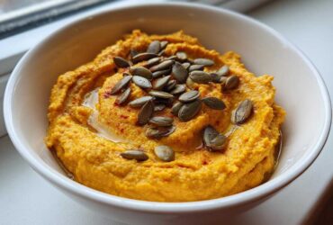 A bowl of creamy Vegan Pumpkin Hummus topped with pumpkin seeds and a sprinkle of paprika.
