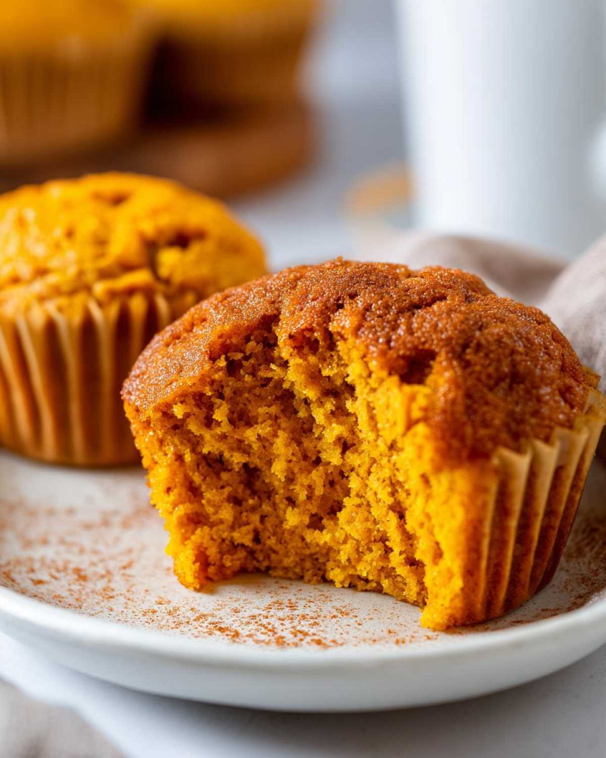 Close-up of a vegan pumpkin muffin with a bite taken out, showing its moist and fluffy texture.