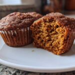 Close-up of two delicious vegan pumpkin muffins on a white plate, one is bitten into.