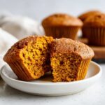 Close-up of a vegan pumpkin muffin, split in half, revealing a moist and fluffy interior.