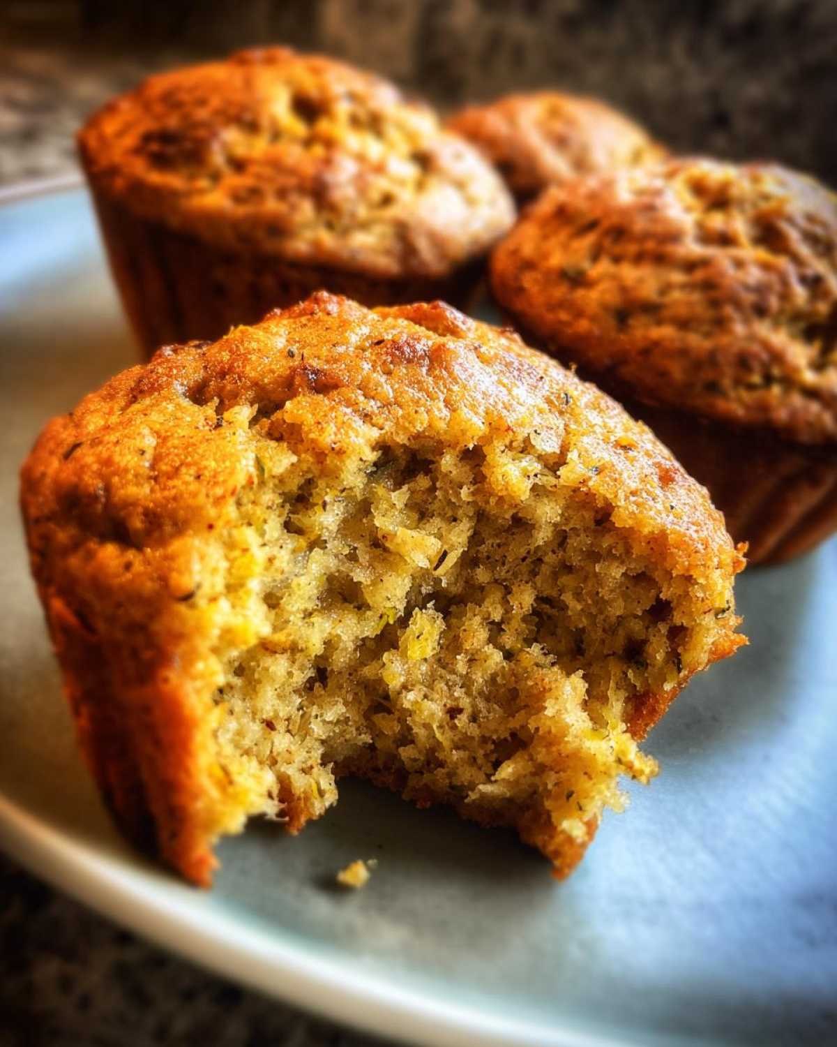 Close-up of a delicious vegan zucchini muffin with a bite taken out, showing its moist and tender crumb.