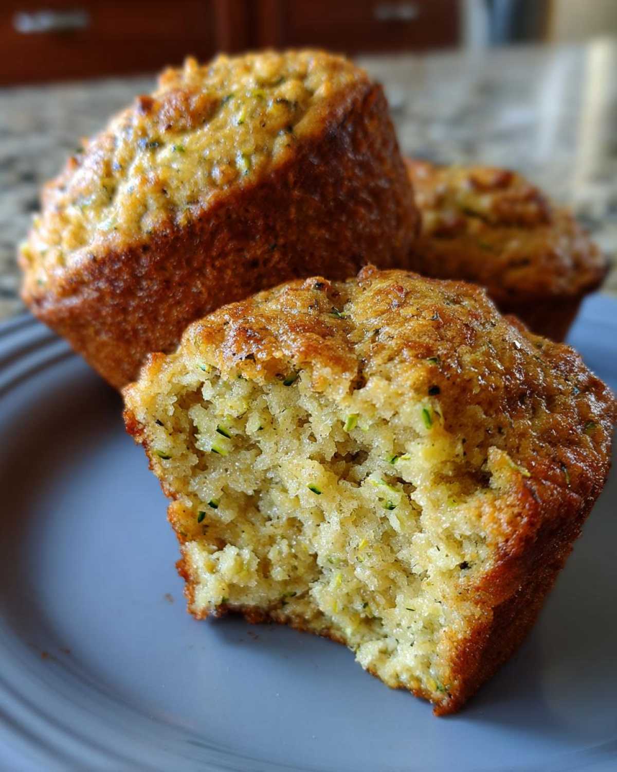Close-up of a vegan zucchini muffin, with one muffin broken in half to reveal the moist interior with visible zucchini shreds.