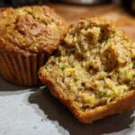 Close-up of two vegan zucchini muffins on a plate, one is broken in half revealing the moist interior with shredded zucchini.
