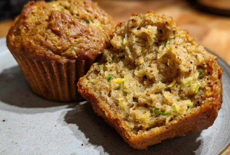 Close-up of two vegan zucchini muffins on a plate, one is broken in half revealing the moist interior with shredded zucchini.