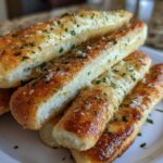 A stack of freshly baked, golden brown breadsticks seasoned with garlic butter, Parmesan cheese, and chopped parsley.