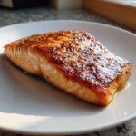 A close-up of a perfectly cooked, glazed air fryer salmon fillet resting on a white plate.