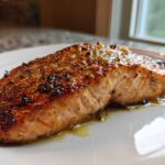 Close-up of a glazed, perfectly cooked air fryer salmon fillet resting on a white plate.