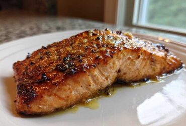 Close-up of a glazed, perfectly cooked air fryer salmon fillet resting on a white plate.