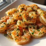 Close-up of juicy, seasoned air fryer shrimp piled on a white plate, glistening with butter and herbs.