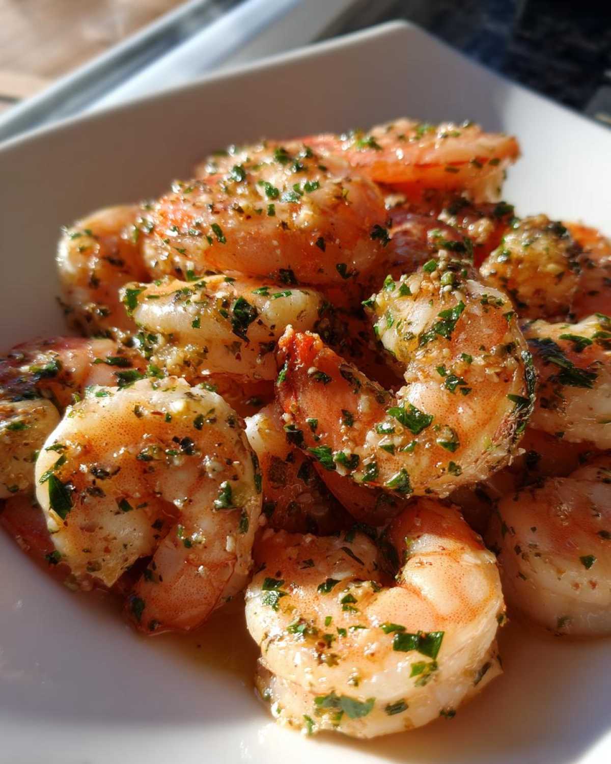 A close-up of juicy, seasoned air fryer shrimp piled on a white plate, glistening with butter and parsley.