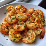 A close-up of juicy, golden-brown air fryer shrimp seasoned with garlic and fresh parsley on a white plate.
