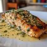 Close-up of a perfectly cooked fillet from a baked salmon recipe, glistening in a garlic butter sauce topped with fresh parsley.