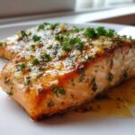 Close-up of a perfectly cooked baked salmon recipe fillet topped with garlic, butter, and fresh parsley.