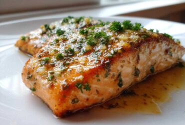Close-up of a perfectly cooked baked salmon recipe fillet topped with garlic, butter, and fresh parsley.