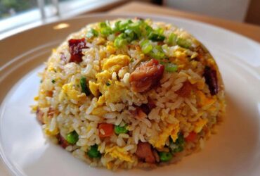 A perfectly molded serving of chicken fried rice with visible chunks of chicken, scrambled egg, peas, and carrots, topped with green onions.