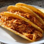 Three crispy, golden corn shells generously filled with saucy, shredded chicken for amazing chicken tacos.
