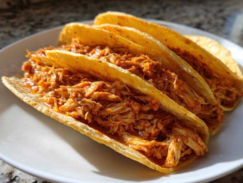 Three crispy, golden corn shells generously filled with saucy, shredded chicken for amazing chicken tacos.