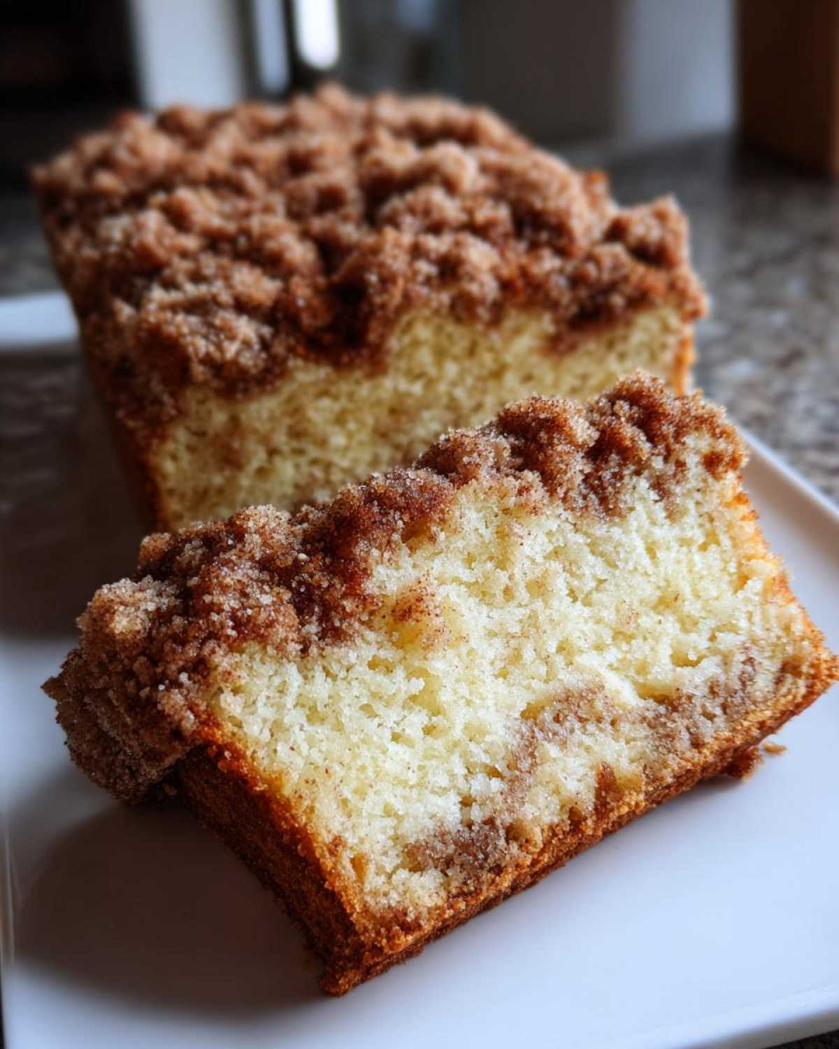 Close-up of a slice of moist coffee cake showing a thick cinnamon crumb topping and soft interior.