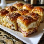 Close-up of baked Ham and Cheese Sliders on a white platter, showing melted cheese and everything bagel seasoning.