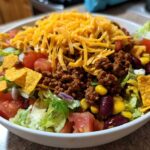 A generous serving of taco salad featuring seasoned ground beef, shredded cheese, lettuce, tomatoes, corn, beans, and tortilla chips.