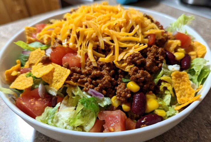 A generous serving of taco salad featuring seasoned ground beef, shredded cheese, lettuce, tomatoes, corn, beans, and tortilla chips.
