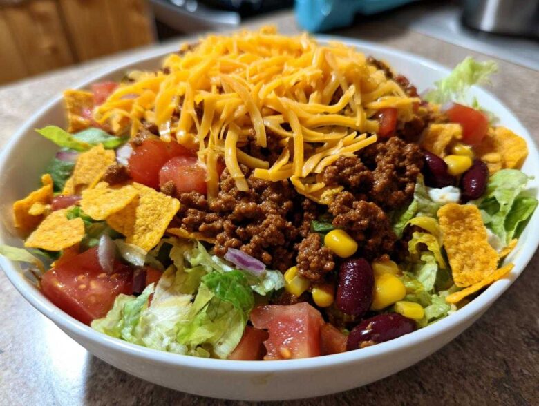 A generous serving of taco salad featuring seasoned ground beef, shredded cheese, lettuce, tomatoes, corn, beans, and tortilla chips.
