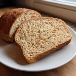 A loaf of homemade whole wheat bread, sliced, sitting on a white plate.