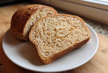 A loaf of homemade whole wheat bread, sliced, sitting on a white plate.