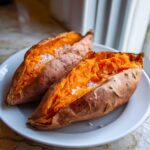 Two halves of perfectly cooked baked sweet potatoes, showing fluffy orange flesh topped with coarse sea salt.