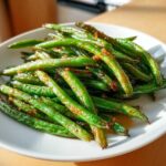 Close-up of bright green, blistered chinese green beans with garlic sauce piled on a white plate.