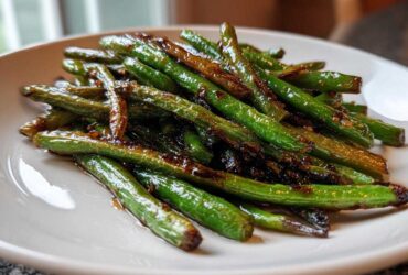 A close-up of blistered chinese green beans with garlic sauce piled on a white plate.