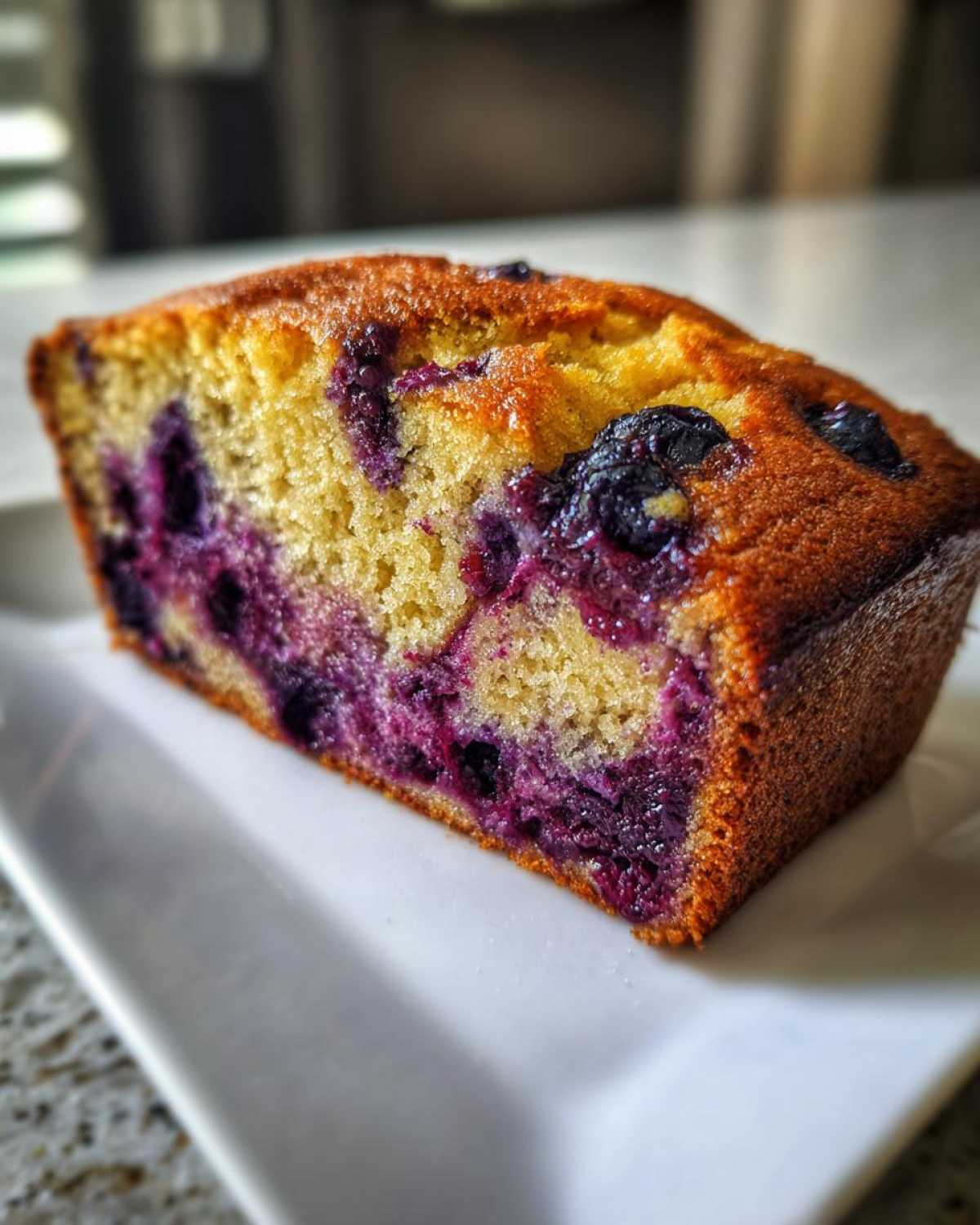 Close-up of a moist slice of blueberry banana bread showing rich purple blueberries baked into the golden crumb.