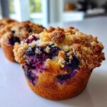 A close-up, low-angle shot of a golden-brown blueberry muffin topped with crunchy streusel, showcasing burst blueberries.