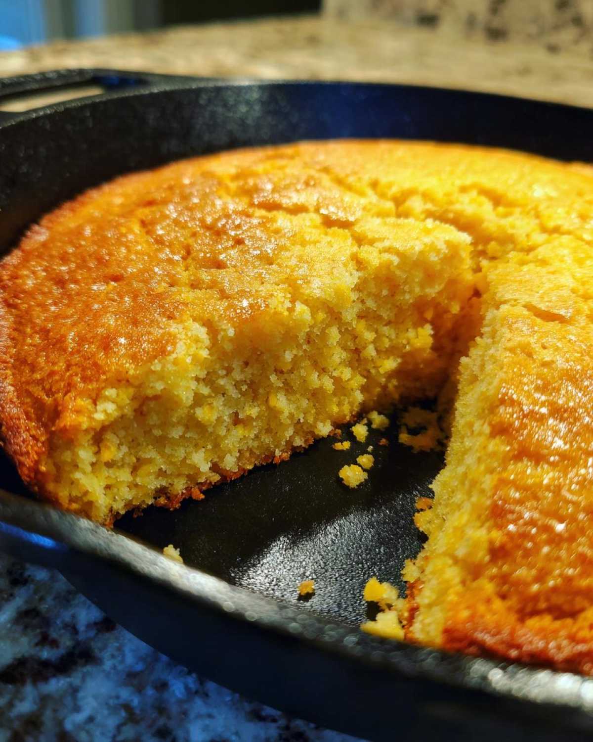 Close-up of golden brown buttermilk cornbread with a slice removed, sitting in a black cast iron skillet.