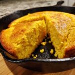 Close-up of a freshly baked buttermilk cornbread, cut into slices inside a black cast iron skillet.