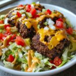 Close-up of a delicious cheeseburger bowl featuring seasoned beef patties, melted cheese, lettuce, tomatoes, onions, and special sauce.