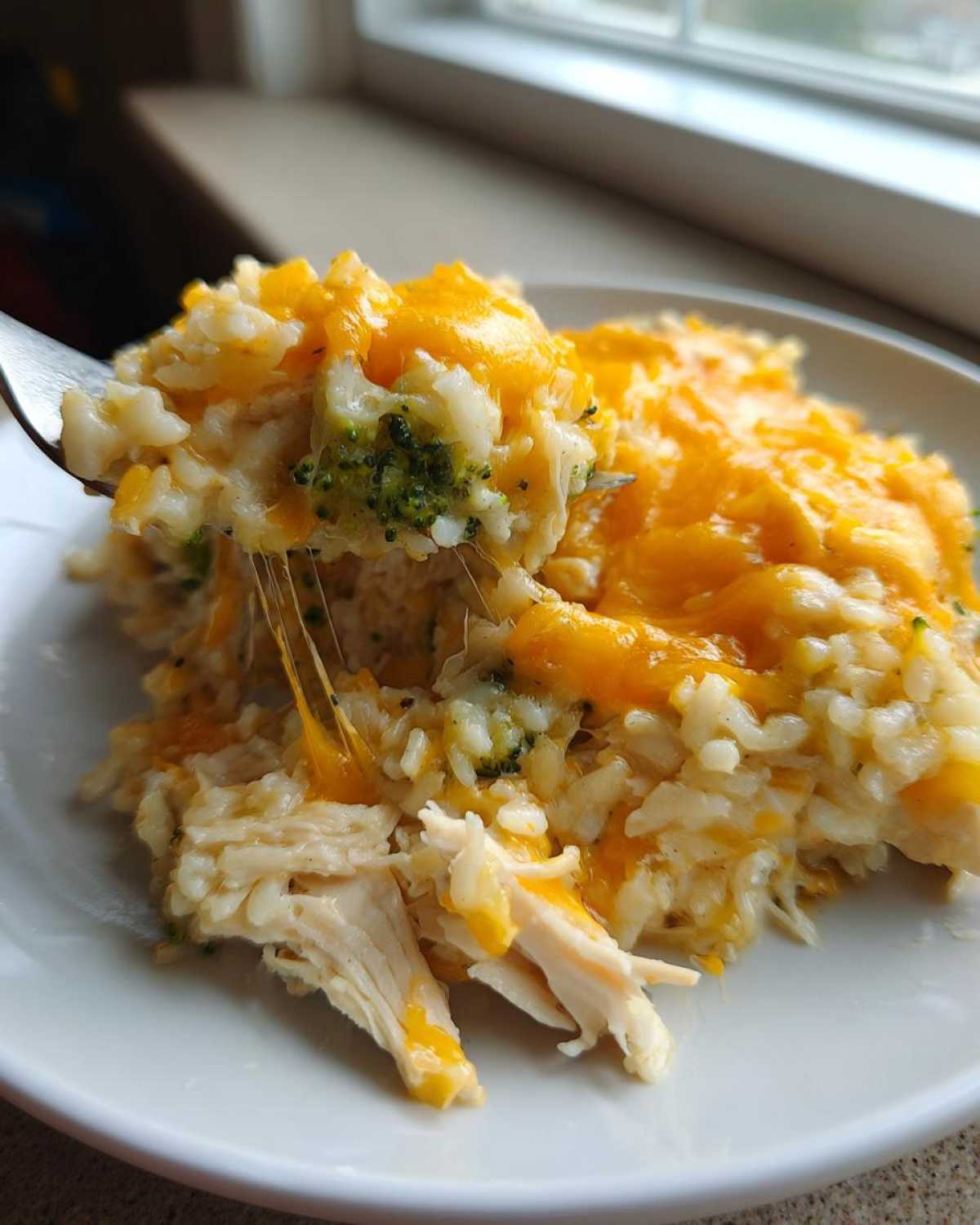 Close-up of a fork lifting cheesy chicken and rice, showing melted cheese stretching between the fork and the plate.