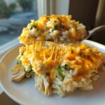 A spoonful of cheesy chicken and rice lifted from a plate, showing long, melted cheese strings.