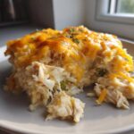 A close-up serving of cheesy chicken and rice casserole with melted cheddar cheese topping.