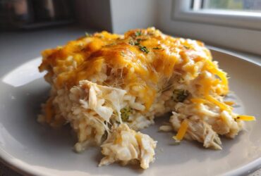A close-up serving of cheesy chicken and rice casserole with melted cheddar cheese topping.