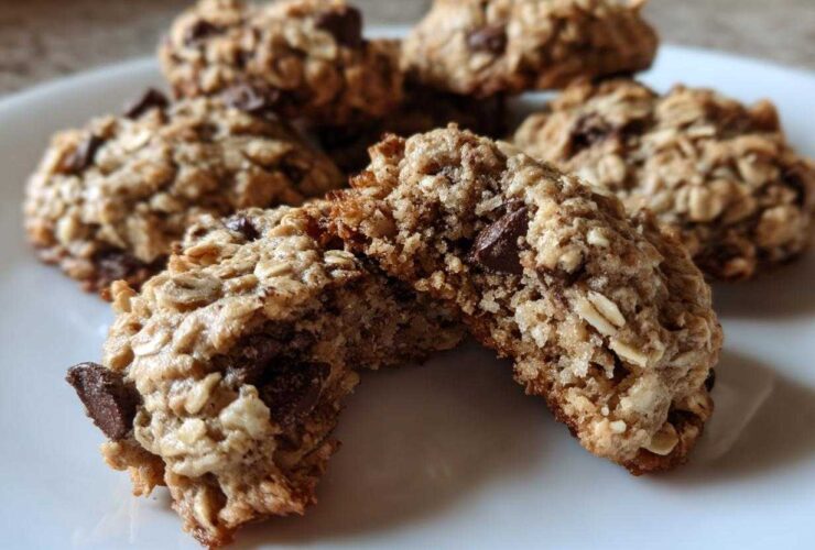 A chocolate chip oatmeal cookie broken in half, showing its chewy interior texture on a white plate.