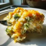 A close-up of a serving of creamy chicken broccoli rice casserole topped with melted cheddar cheese.