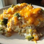 A close-up serving of creamy chicken broccoli rice casserole topped with melted cheddar cheese on a white plate.