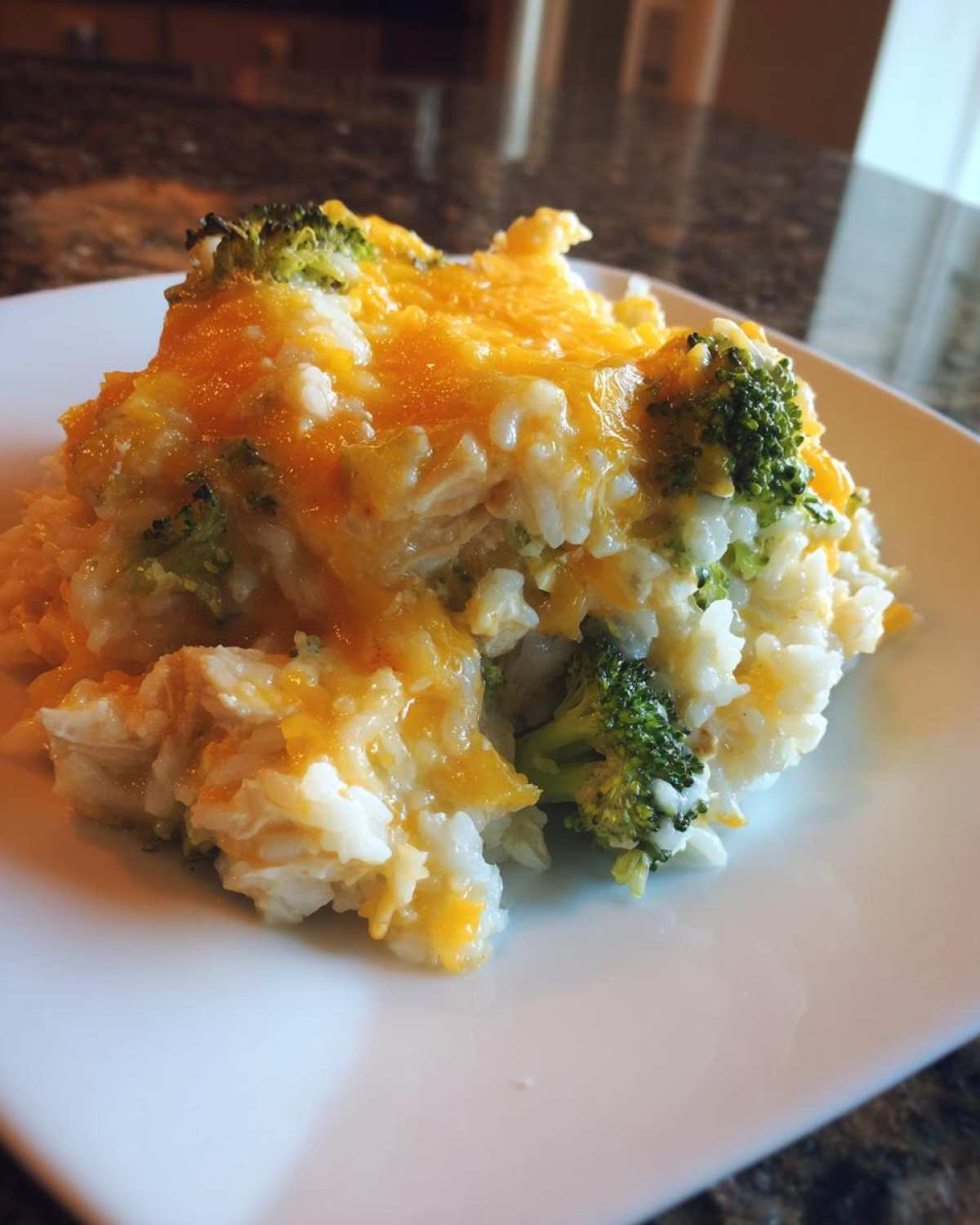 A close-up serving of creamy chicken broccoli rice casserole topped with melted cheddar cheese.