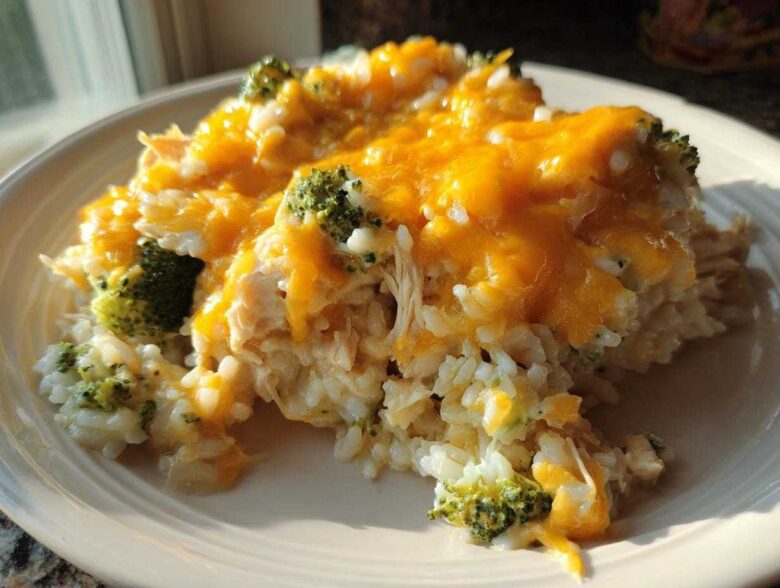 A close-up serving of creamy chicken broccoli rice casserole topped with melted cheddar cheese on a white plate.