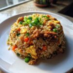 A mound of savory chicken fried rice featuring scrambled egg, carrots, peas, and topped with fresh green scallions.