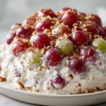 A mound of creamy grape salad topped with red and green grapes and chopped pecans, resembling the Chicken Salad Chick grape salad.